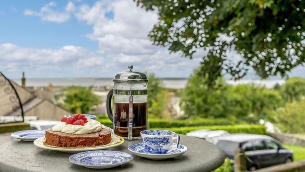 A table with a cake, a coffee pot, and a cup on a terrace with a view of the sea. - 5 Bed in Askam-in-furness (oc-89226) (Kirkby Ireleth)