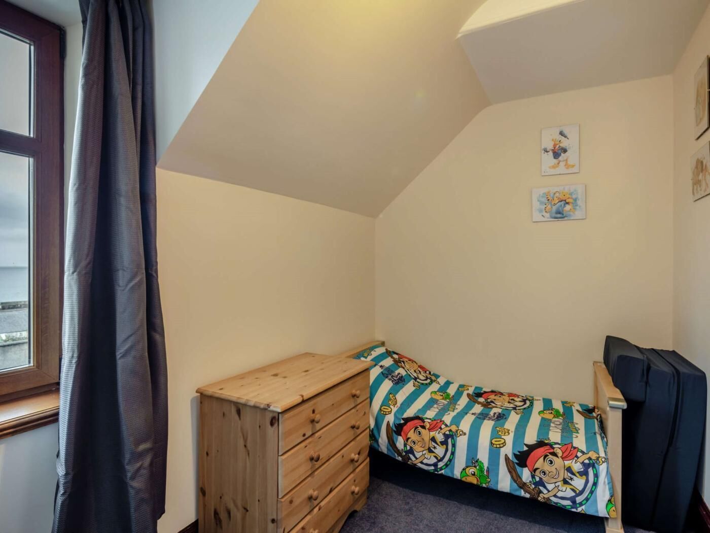 Quarto com uma cama de solteiro, uma cômoda de madeira e duas imagens penduradas na parede.