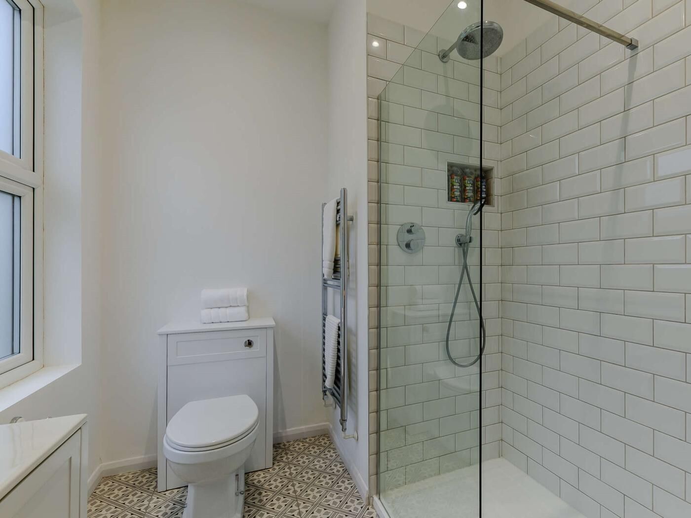 A bathroom with a toilet, a glass shower enclosure, and a tiled floor.