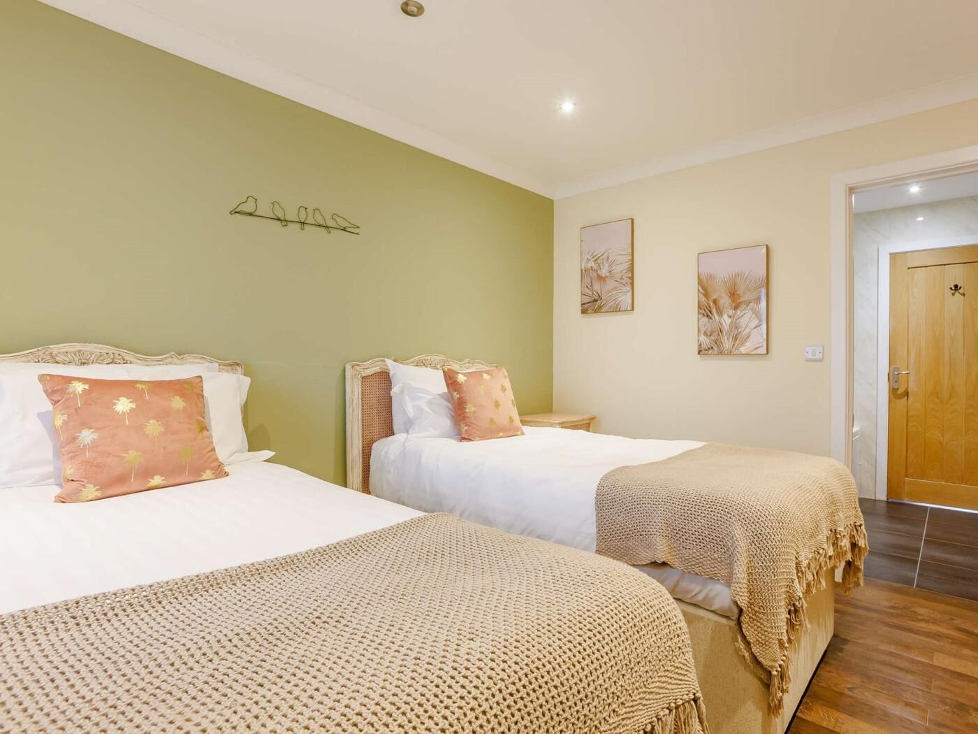 A room with two beds, a green wall, and two framed pictures.