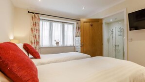Ein Hotelzimmer mit zwei Betten, einem Fernseher, einer Dusche und einem Fenster mit Vorhängen.