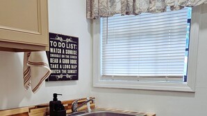 Eine Küche mit Holzschränken, einem Spülbecken, einem Fenster mit Jalousien und einem Schild mit der Aufschrift 'To Do List'.