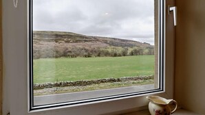 A window with a view of a green field and a stone wall, a white door, and a ceramic pitcher on the windowsill. - 3 Bed in Brampton (oc-89994) (Slaggyford)