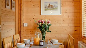 Une table de salle à manger en bois, ornée d’un vase de fleurs, d’une carafe de jus d’orange et de bols de céréales.