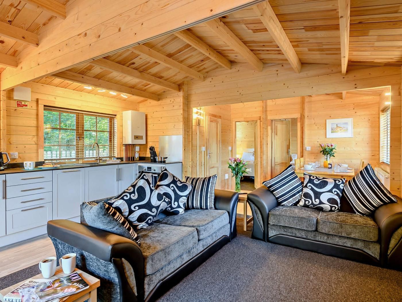 A cozy cabin interior with a wooden ceiling, a kitchenette, a dining area, and a seating area with a sofa and armchairs.
