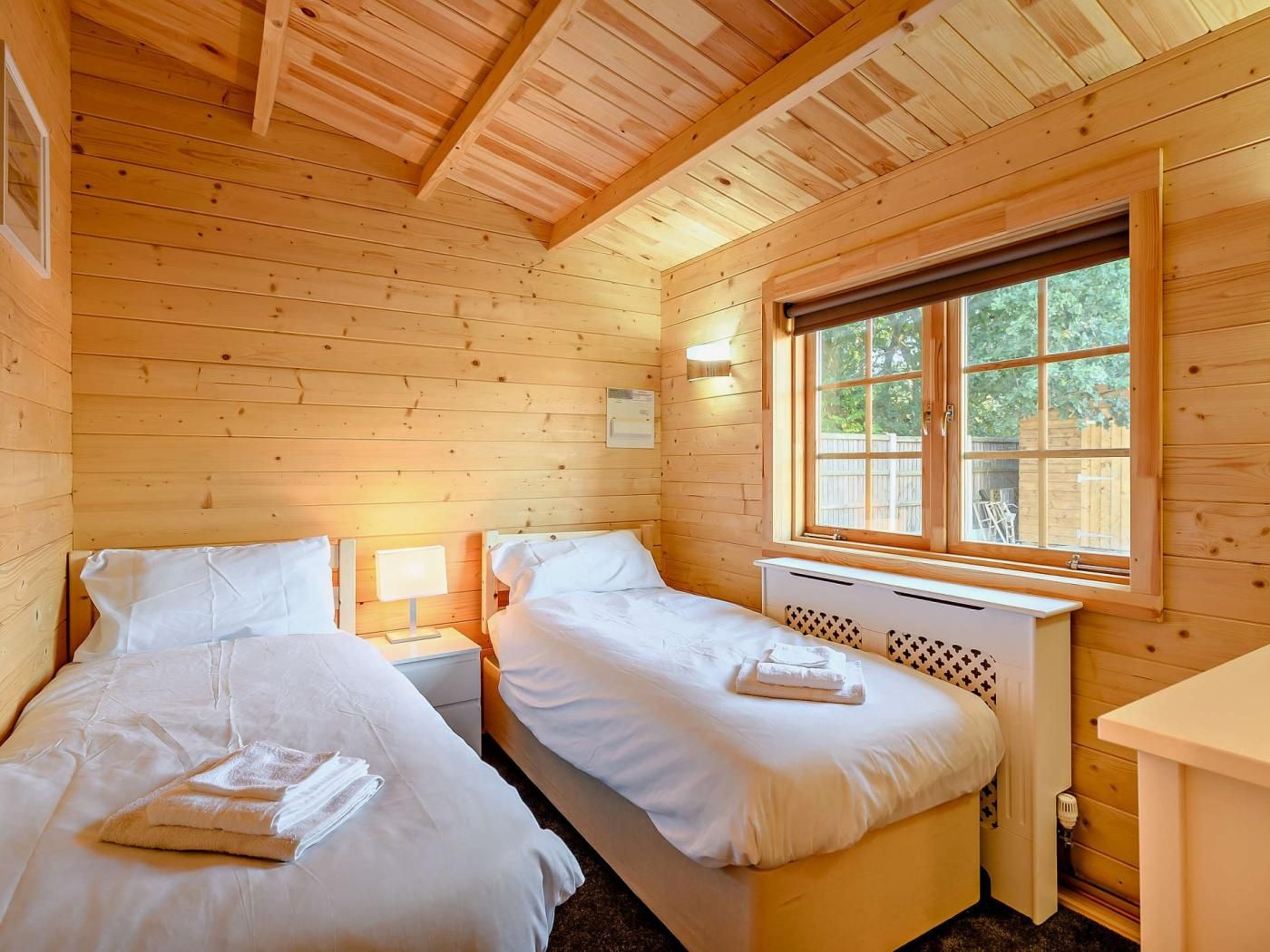 A wooden cabin room with two beds, a window, and a small desk.