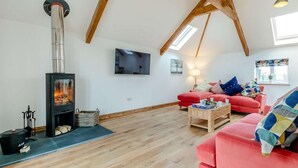 Ein Loft-Zimmer mit Kaminofen, einem roten Sofa, einem Fernseher und einer Holzbalkendecke.