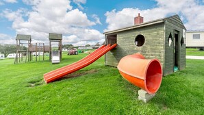 Ein Spielplatz mit Rutsche, Spielhaus und einer großen, orangefarbenen Röhre.