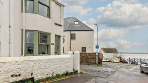 A two-story building with a white exterior and green window frames, a stone wall in front, and a parking area with a blue sign. - 3 Bed in Bideford (oc-89991) (Appledore)