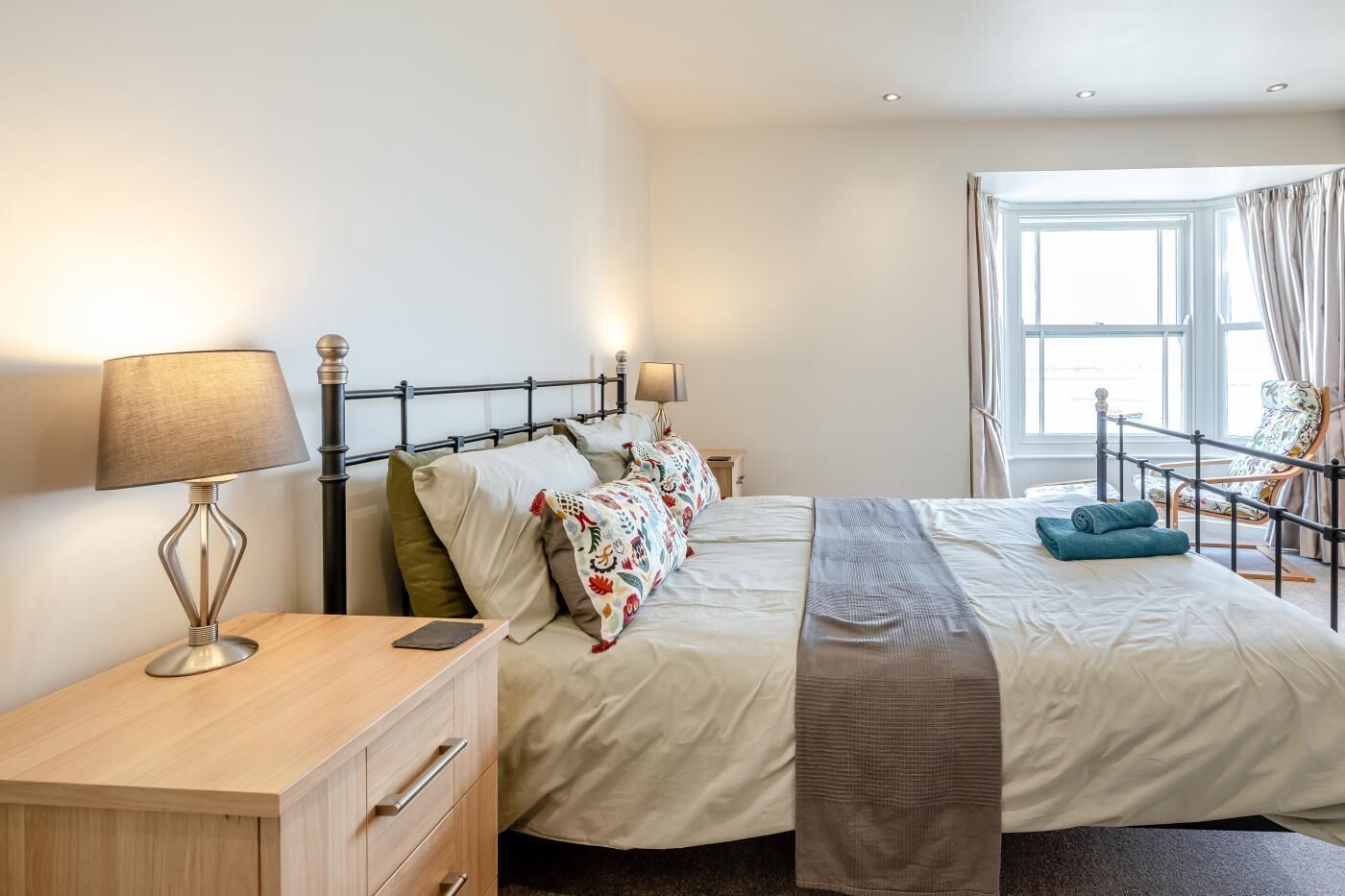 A bedroom with a bed, bedside tables, a desk, and a window with curtains.