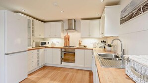 A compact kitchen with white cabinets, a microwave, a stove, and a sink. - 3 Bed in Bideford (oc-89991) (Appledore)
