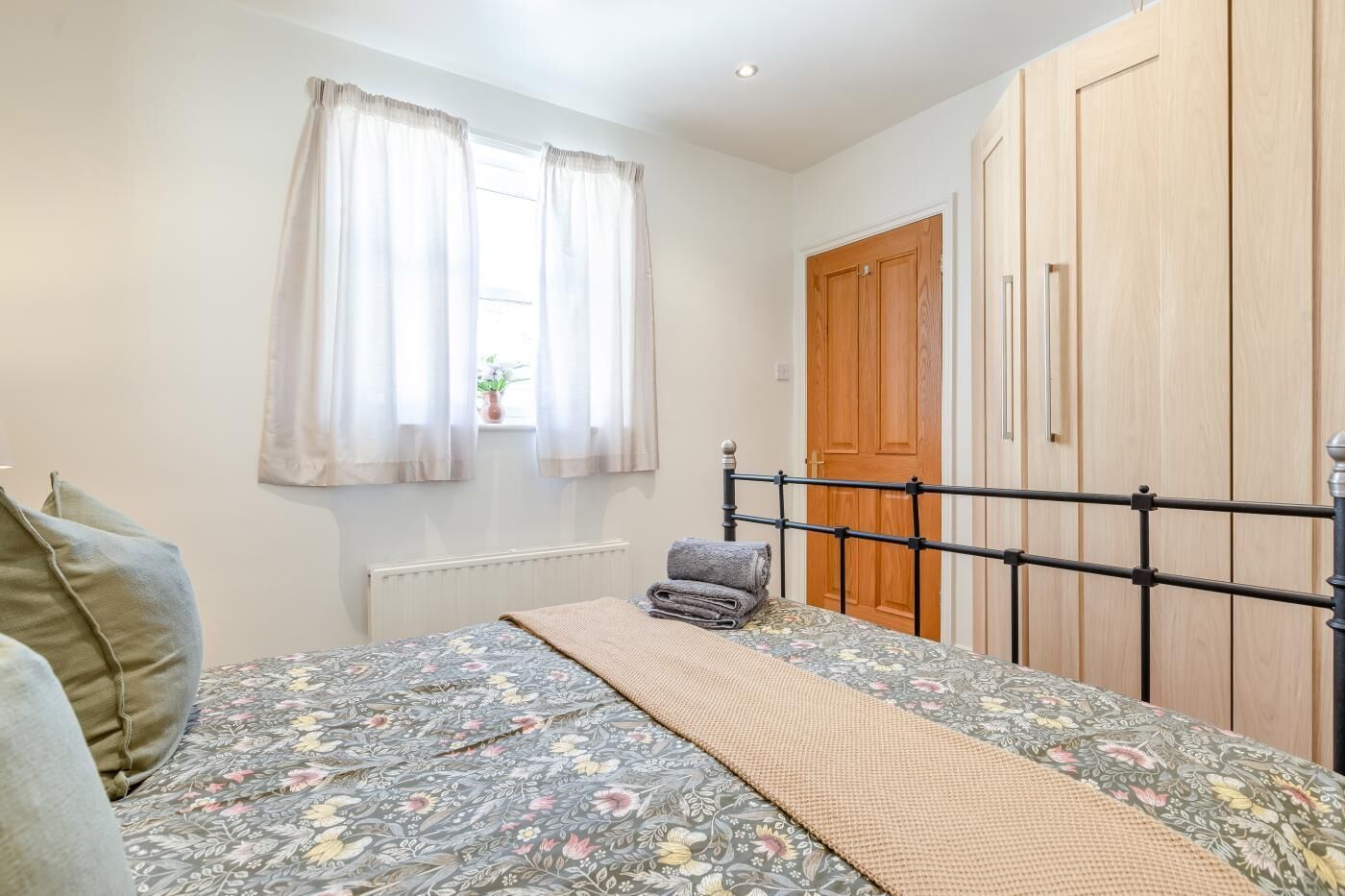 A bedroom with a bed, a radiator, a window with curtains, a wooden door, and a wardrobe.