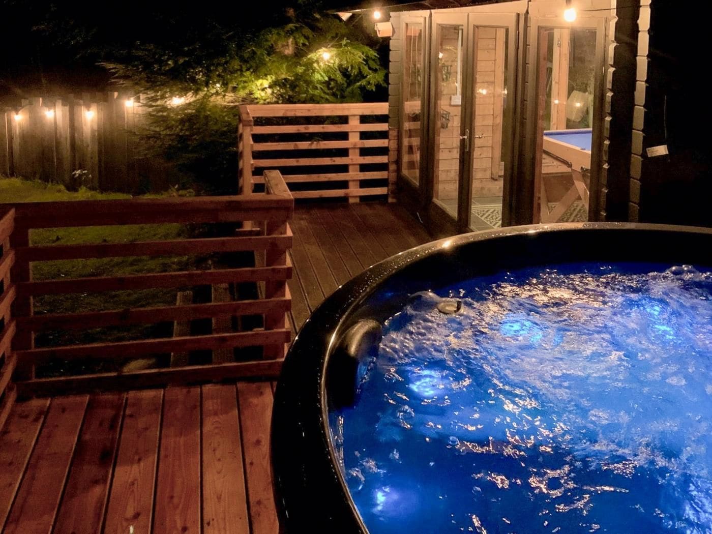 A hot tub on a wooden deck with a glass enclosure and a wooden fence.