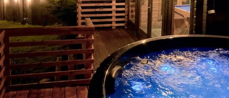 A hot tub on a wooden deck with a glass enclosure and a wooden fence.
