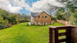 Uma cabana de madeira com telhado inclinado, rodeada por um jardim bem cuidado e uma cerca de madeira.