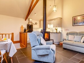 Ein gemütliches Wohnzimmer mit Kamin, eine Essecke mit gedecktem Tisch für das Frühstück und eine Küche im Hintergrund.