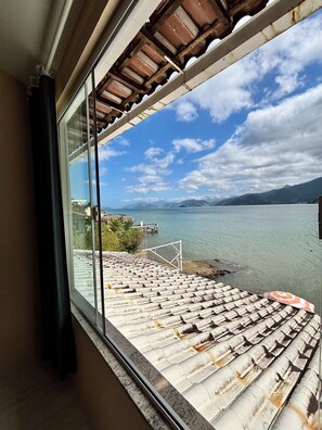 A view from a window overlooking a body of water with a dock and mountains in the distance. - Vrbo Property (Mangaratiba)