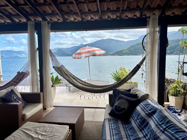 Un fauteuil suspendu et un canapé placés face à un lac, avec des montagnes en arrière-plan.