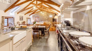 A kitchen with wooden beams, a stone wall, and a dining area with chairs and a table. - 4 Bed in Kingsbridge (oc-90027) (South Huish)
