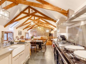 Eine Küche mit Holzbalken, einer Steinwand und einem Essbereich mit Stühlen und Tisch.