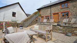 A stone building with a white exterior, a wooden bench, and a small table with a cushion. - 4 Bed in Kingsbridge (oc-90027) (South Huish)