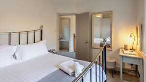 Habitación de hotel con cama, escritorio, espejo y baño visible a través de una puerta abierta.