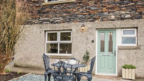 Un edificio de piedra con una puerta verde, una ventana con marco blanco y una mesa con sillas afuera.