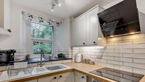 Una cocina moderna con armarios blancos, una campana de acero inoxidable, un horno empotrado y una ventana con vistas a la vegetación.