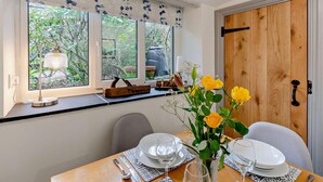 Un comedor con una mesa dispuesta para dos, una ventana que da a zonas verdes, y una puerta de madera.