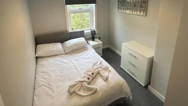 Un dormitorio con cama, mesita de noche, cómoda, ventana con vista y lámpara colgante.