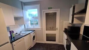 Cocina compacta con armarios blancos, lavadora y ventana.