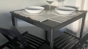Una pequeña mesa de comedor con dos tazones blancos y dos copas de vino, junto a una silla negra.