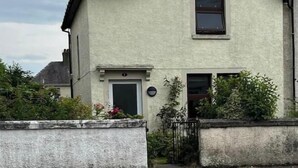 Una casa de dos pisos con techo a dos aguas, una puerta principal y un ventanal pequeño.