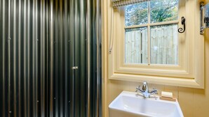 Un baño con un lavamanos blanco, una ventana que da a una valla de madera y un box de ducha de metal.