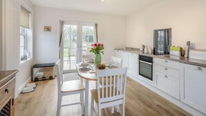 Una cucina moderna con pensili bianchi, un tavolo da pranzo con sedie, un vaso con fiori e vista panoramica attraverso una porta in vetro.