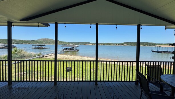 Eine überdachte Terrasse mit Blick auf einen See, angestellte Boote und ferne Hügel.