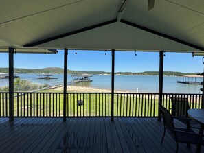 Une terrasse couverte offrant une vue sur un lac, des bateaux amarrés et des collines lointaines.