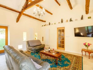A living room with a sofa, a coffee table, a fireplace, a chandelier, and a television mounted on the wall. - 1 Bed in Conwy (oc-90040) (Ty'n-y-groes)