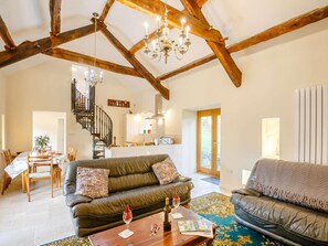 A spacious living room with a high ceiling, exposed wooden beams, a chandelier, a staircase, and a dining area. - 1 Bed in Conwy (oc-90040) (Ty'n-y-groes)