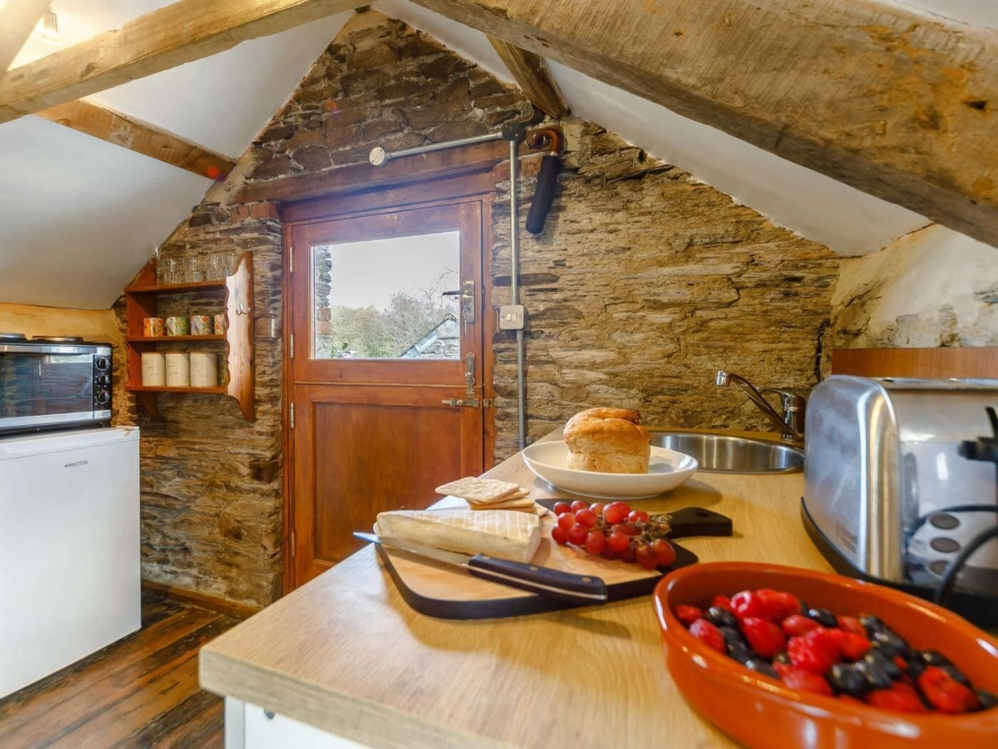A cozy kitchen with a stone wall, wooden beams, a microwave, a toaster, and a bowl of berries.