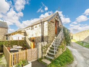 A stone building with a wooden staircase leading to a door, a fenced patio with outdoor furniture, and a clear sky. - 1 Bed in Saltash (oc-90072) (Trerulefoot)