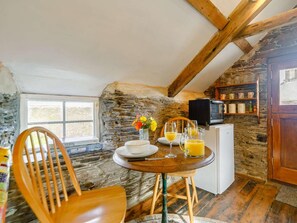 A rustic kitchen with stone walls, wooden beams, a dining table with chairs, a refrigerator, and a window. - 1 Bed in Saltash (oc-90072) (Trerulefoot)