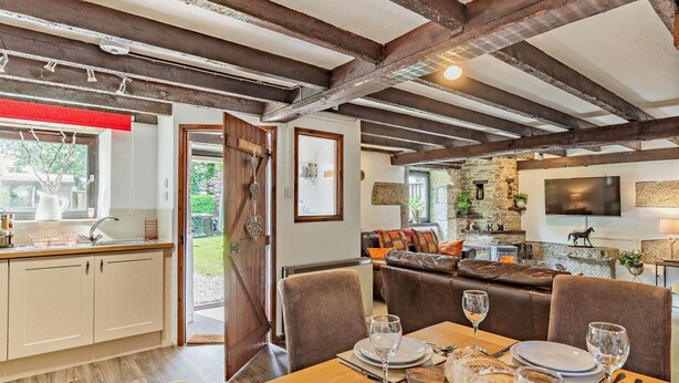 Ein rustikaler Innenraum mit freiliegenden Holzbalken, einem Essbereich mit Holztisch, der für eine Mahlzeit gedeckt ist, und einer gemütlichen Sitzecke mit einer Ledersofa.
