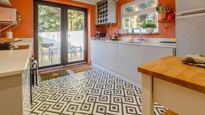 Eine moderne Küche mit einem geometrischen Bodenmuster, einer Schiebetür zu einem Außenbereich und einem Fenster mit Blick auf Grünflächen.