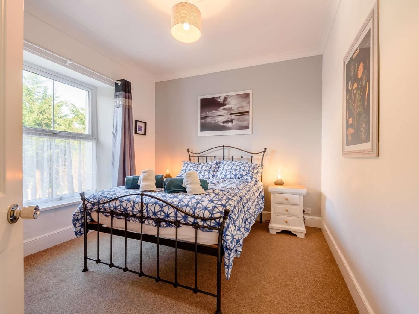 A bedroom with a bed, bedside tables, a window with curtains, and a wall-mounted picture.