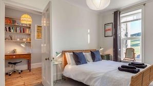 A bedroom with a bed, bedside tables, a desk, a chair, a bookshelf, and a window with a view. - 4 Bed in Woolacombe (oc-90224) (Mortehoe)