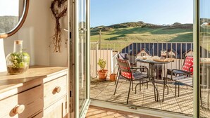 A room with a sliding glass door leading to an outdoor patio with a table, chairs, and potted plants. - 4 Bed in Woolacombe (oc-90224) (Mortehoe)