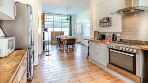 A modern kitchen with a wooden floor, stainless steel appliances, and a dining area with a table and chairs. - 4 Bed in Woolacombe (oc-90224) (Mortehoe)