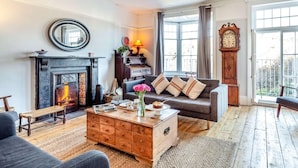 A living room with a fireplace, a sofa, a coffee table, and a large window. - 4 Bed in Woolacombe (oc-90224) (Mortehoe)
