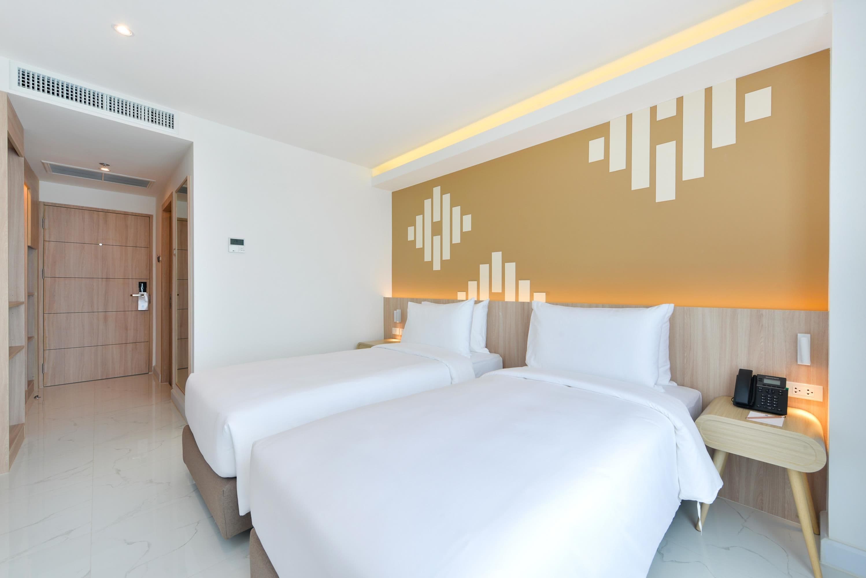 Una camera d'albergo con due letti, un armadio in legno, un comodino con il telefono e una parete con un lampadario geometrico.